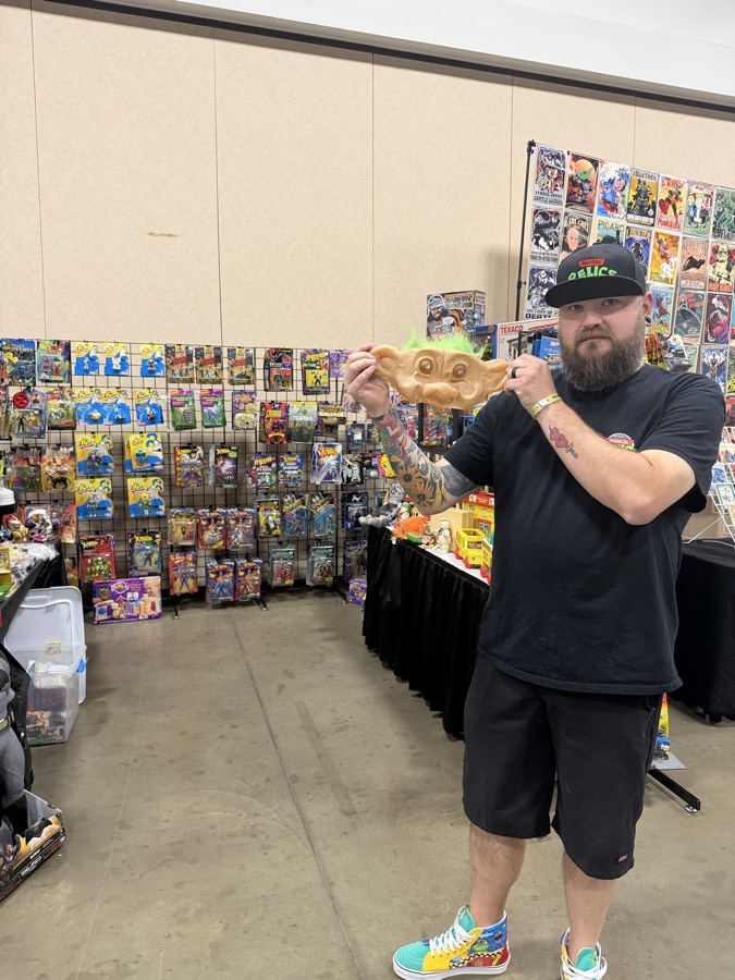 A collector holding up a vintage troll mask in front of a wall of carded action figures