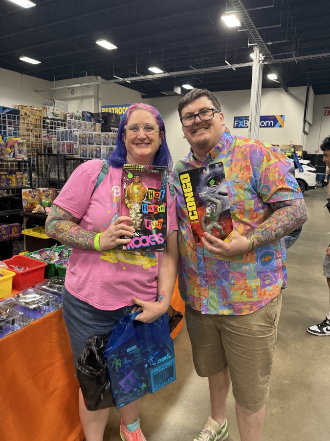 Two collectors grinning while holding a vintage Barbie doll and a Congo action figure they just found