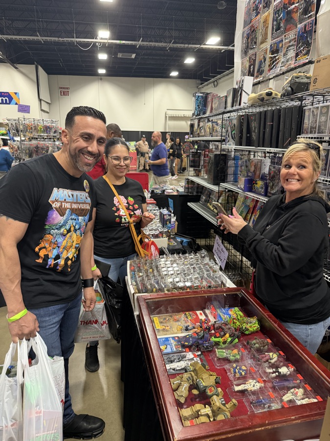 Smiling collectors with shopping bags talking with a vendor over a case of vintage action figures