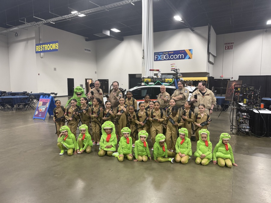 Dozens of kids and adults in Ghostbusters and Slimer costumes posing with an Ecto-1 replica