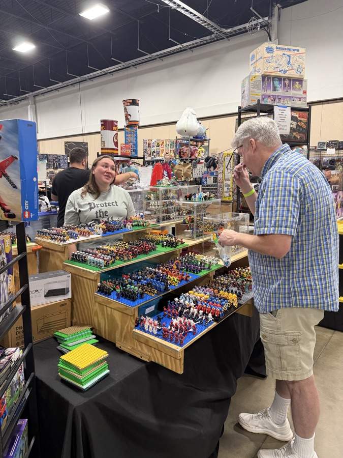 A collector examining a LEGO minifigure at a vendor table filled with hundreds of minifigures