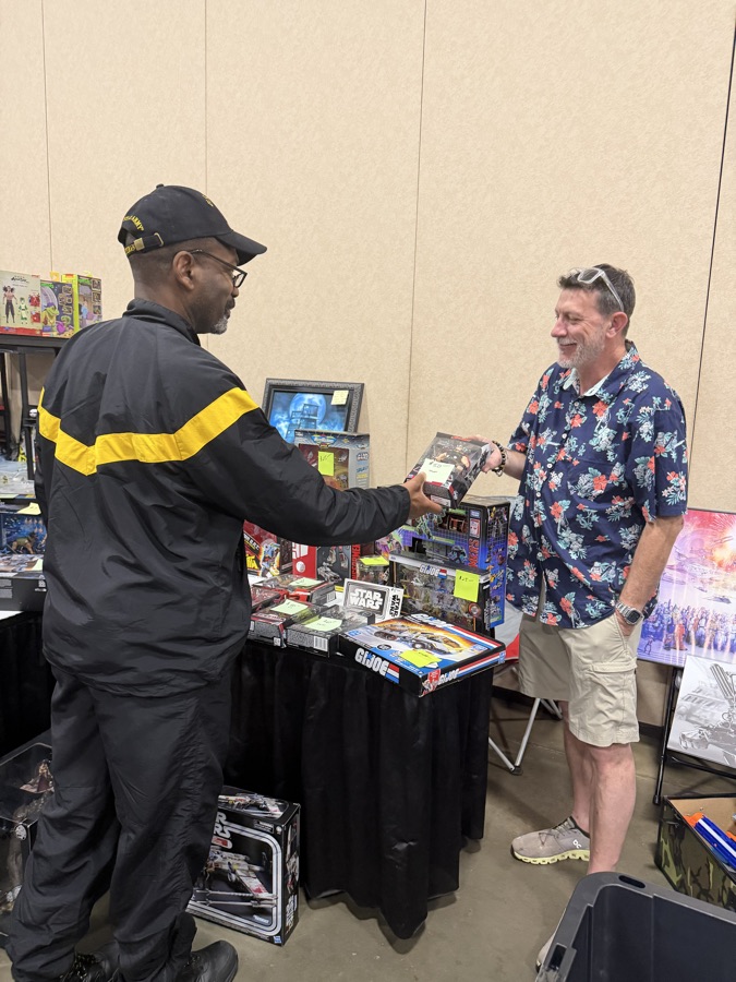 A vendor handing a boxed collectible to a customer at Dominion Toy Con